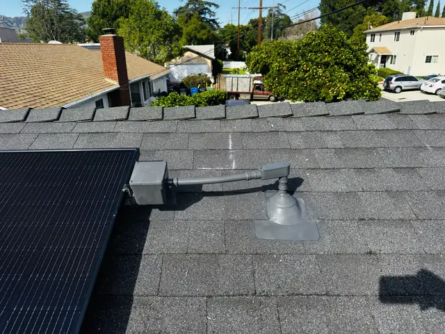 The edge of a solar array on a composition shingle roof with a neighborhood of rooftops and trees beyond, Granada Hills