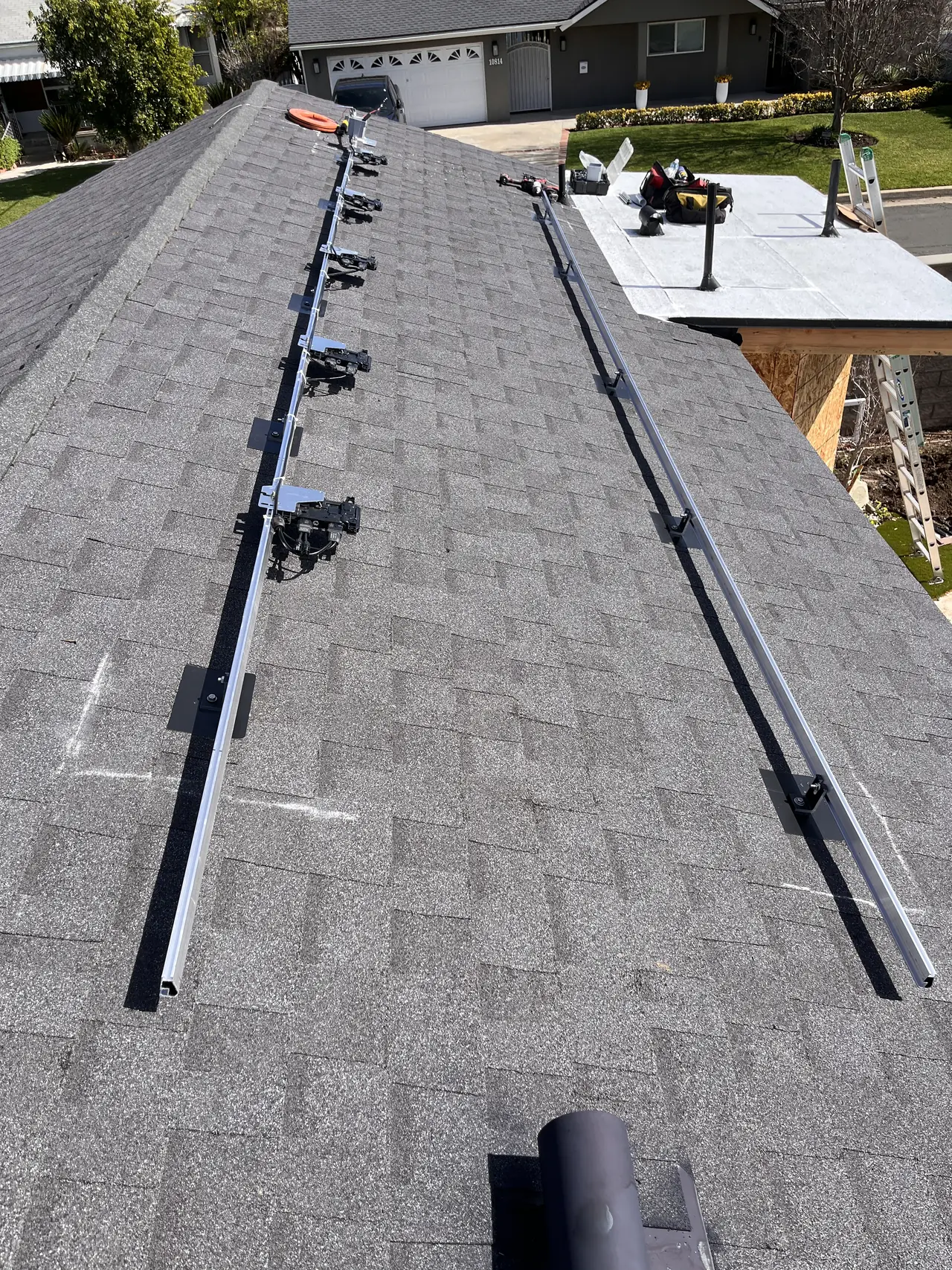 Mounting rails and microinverters running up a shingle roof with a pool and pergola in the yard below, Granada Hills