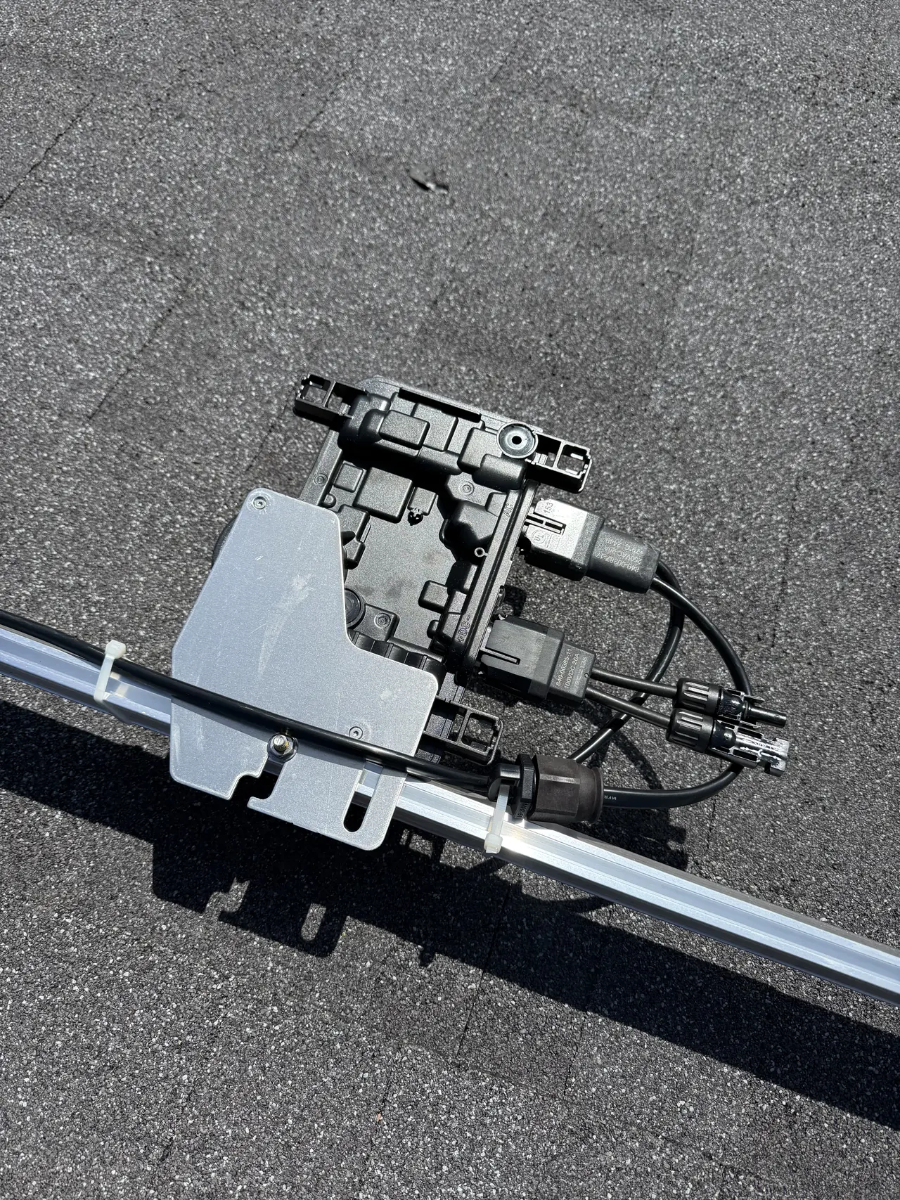 A microinverter clipped to a mounting rail on a shingle roof with its cabling dressed along it, Granada Hills