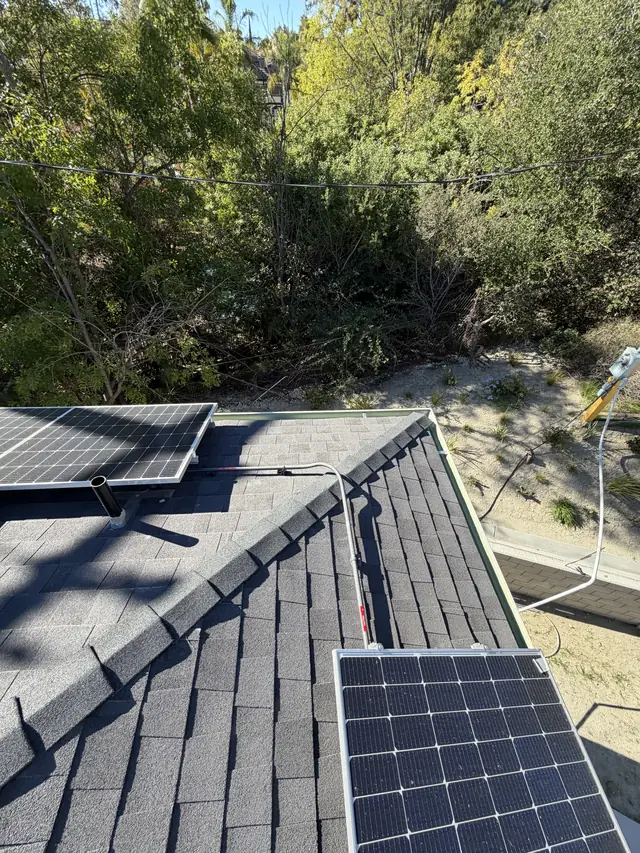 Solar modules on two planes of a shingle roof with a wooded hillside beyond, Granada Hills