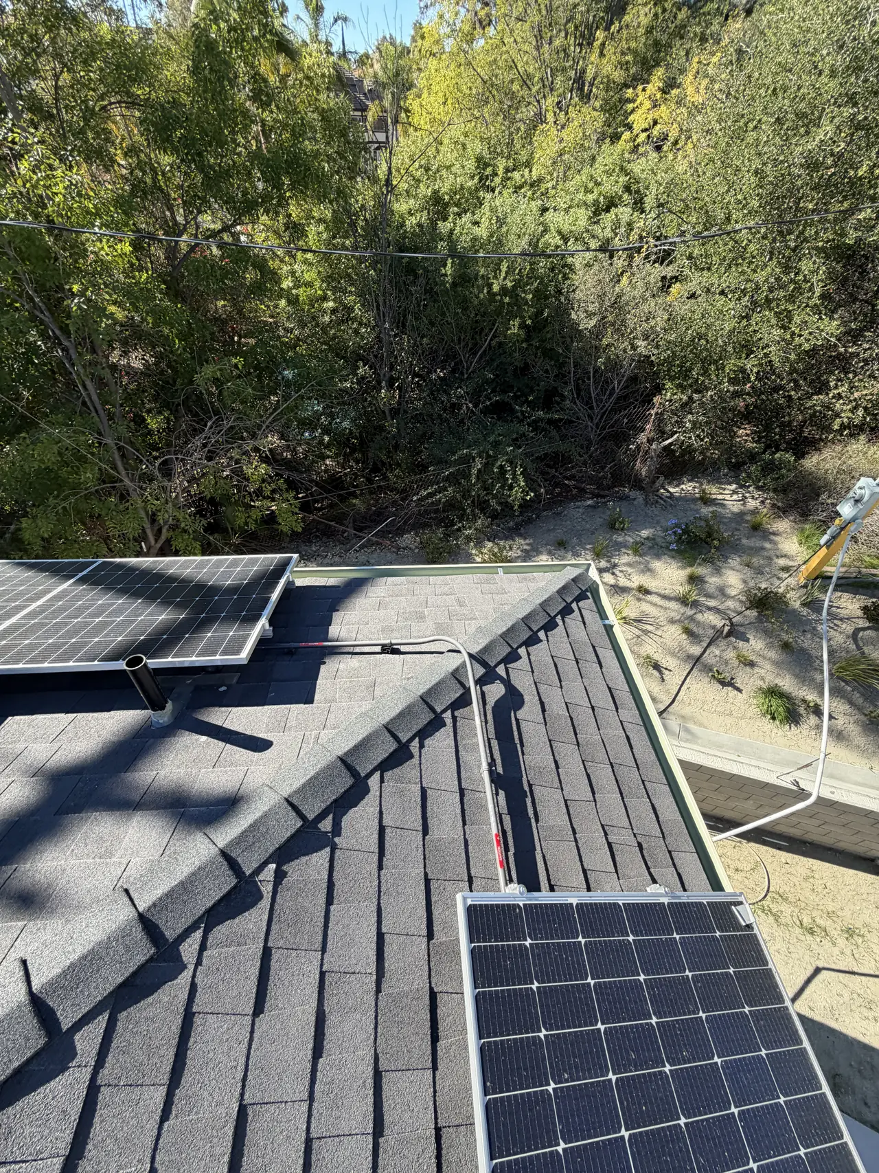 Solar modules on two planes of a shingle roof with a wooded hillside beyond, Granada Hills