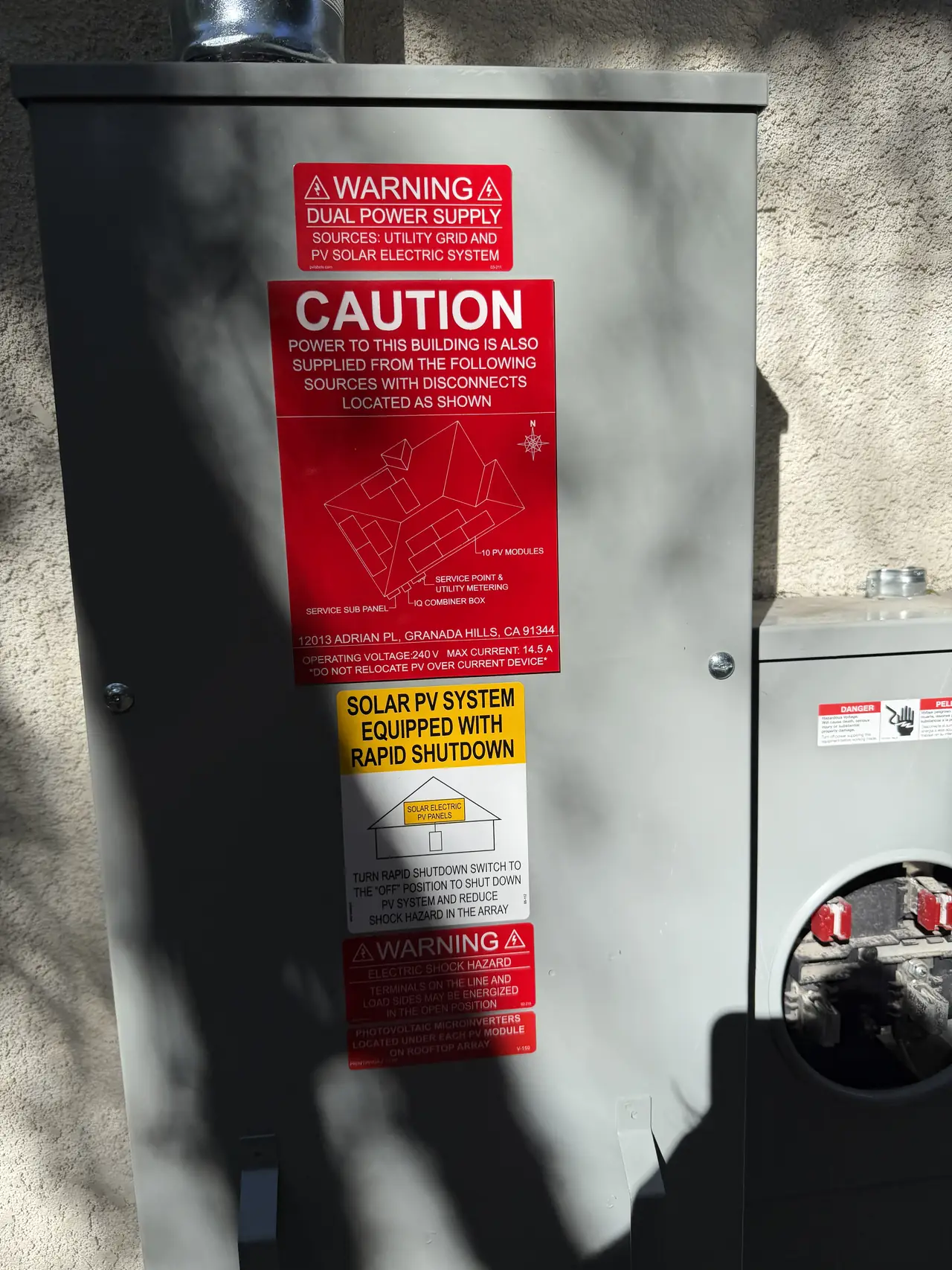 A service panel and solar equipment on a stucco wall with rapid shutdown and warning placards, Granada Hills