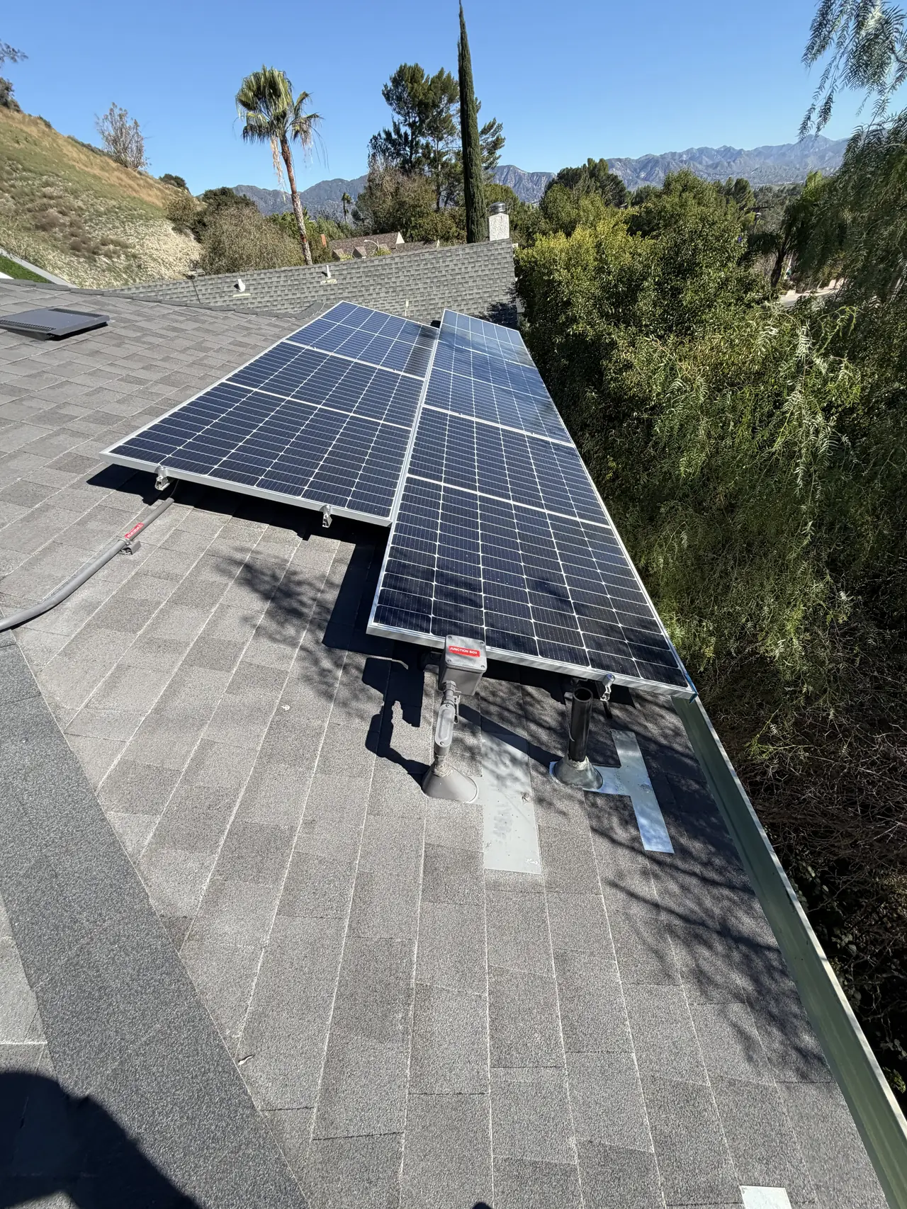 Solar modules on a shingle roof looking out over trees and a hillside, Granada Hills