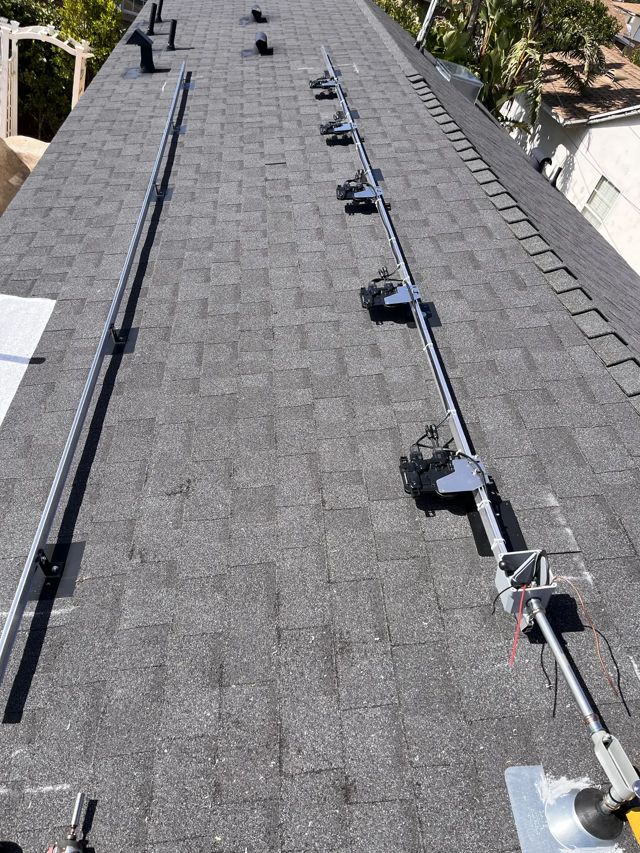 Mounting rails and a microinverter on a shingle roof with a pool in the yard below, Granada Hills