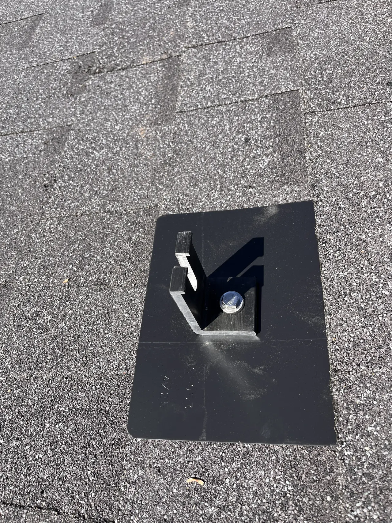 A black flashing plate with an L-foot bolted through it on a composition shingle roof, the bolt set and ready for the rail, Granada Hills