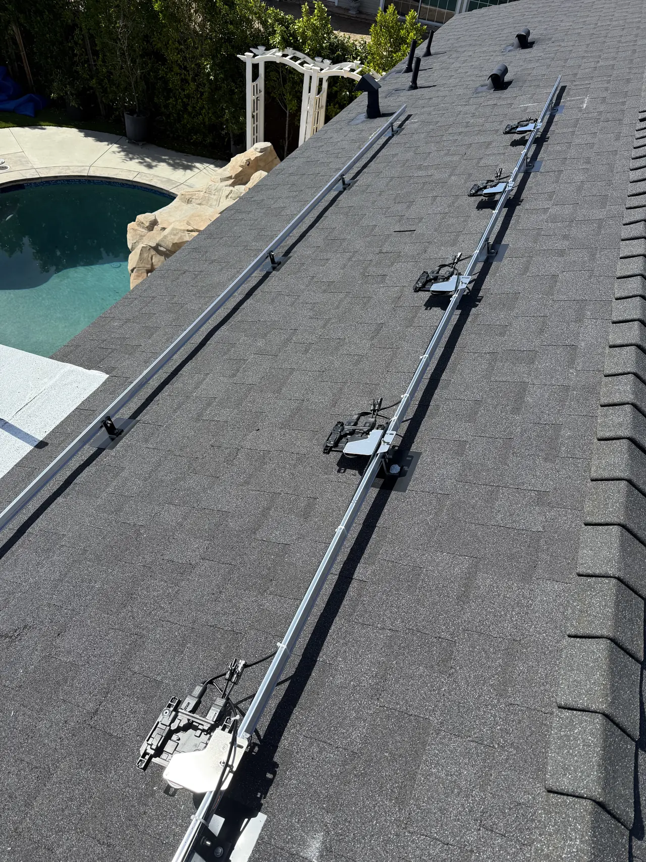 Mounting rails running up a shingle roof with microinverters attached and the neighborhood beyond, Granada Hills