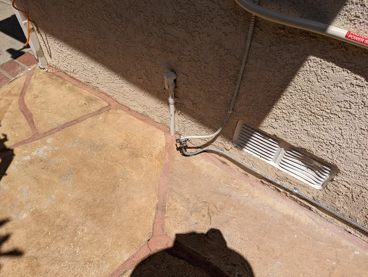 Conduit running down an exterior wall to grade beside a concrete path, Granada Hills