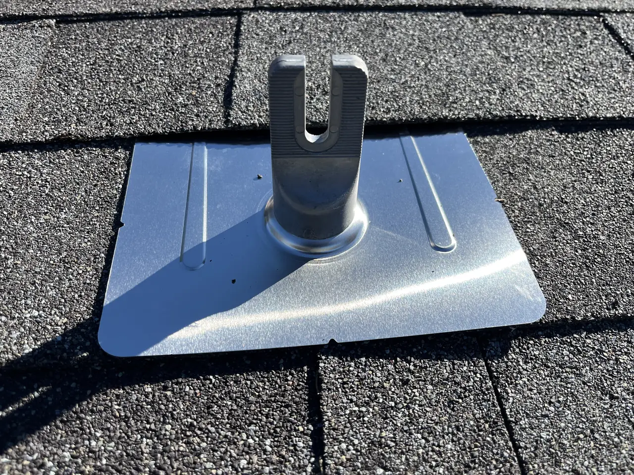 A solar mounting foot standing on a metal flashing plate whose upper edge is slid beneath the shingle course above it, Granada Hills