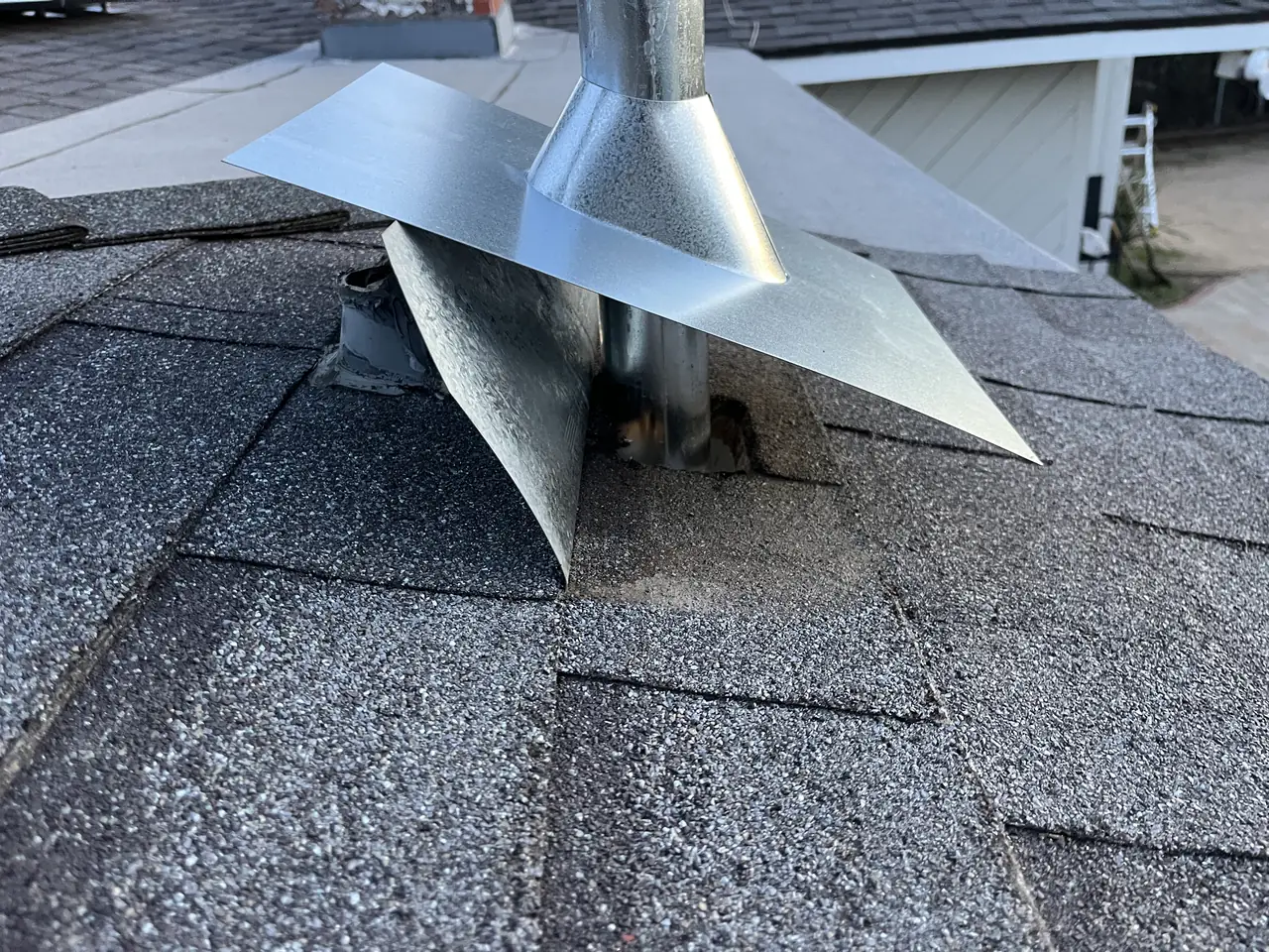 A new galvanized flashing set down over an existing vent pipe, its plate still open before the shingle course goes back over the upslope edge, Granada Hills