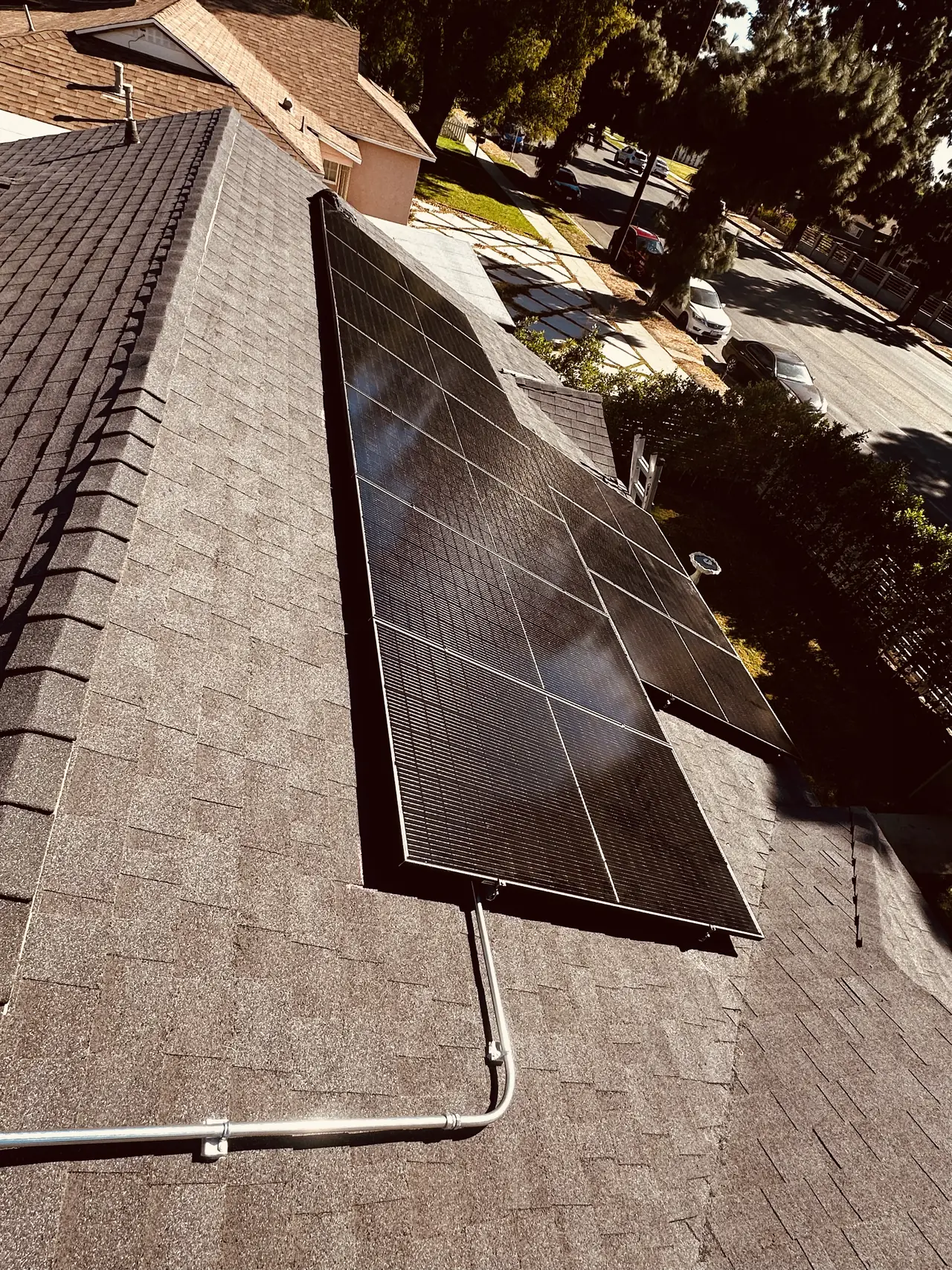 Solar modules on one plane of a hipped composition shingle roof with neighboring houses beyond, Granada Hills
