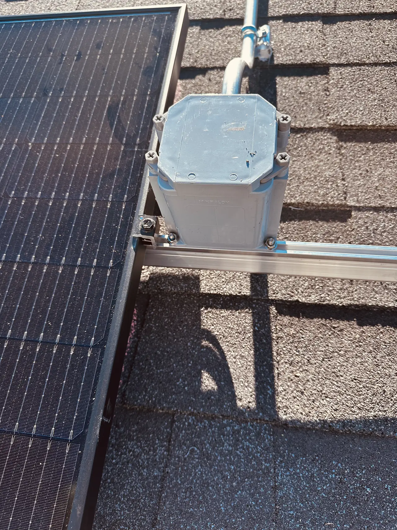 A junction box mounted on the rail beside the edge of a solar module on a shingle roof, Granada Hills