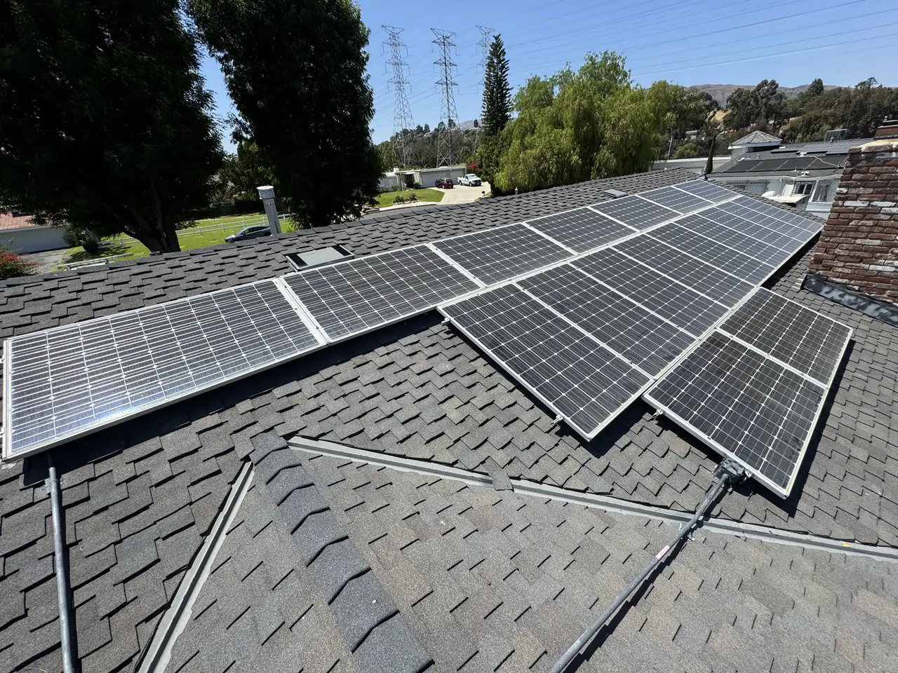 Solar modules across several planes of a shingle roof with trees and neighboring houses beyond, Granada Hills