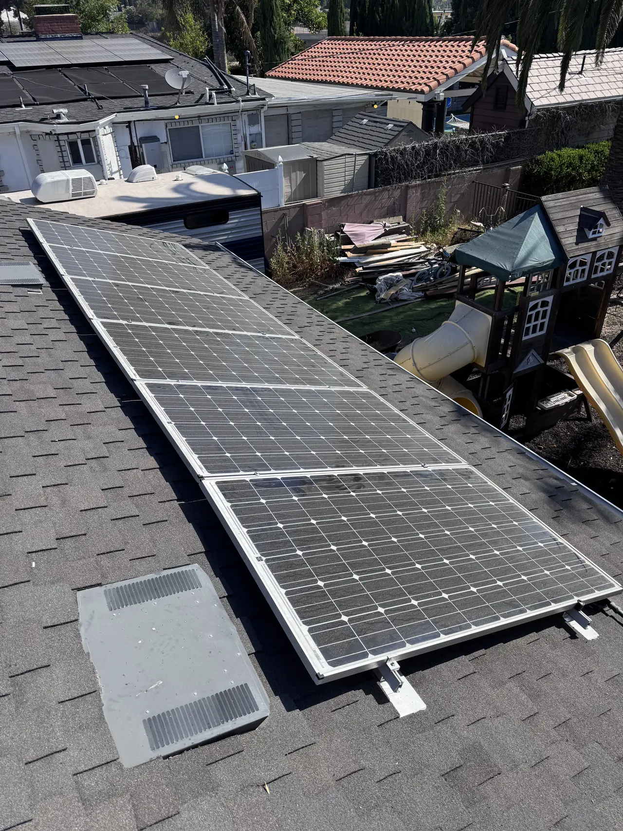 A row of solar modules along the edge of a shingle roof against a clear sky, Granada Hills
