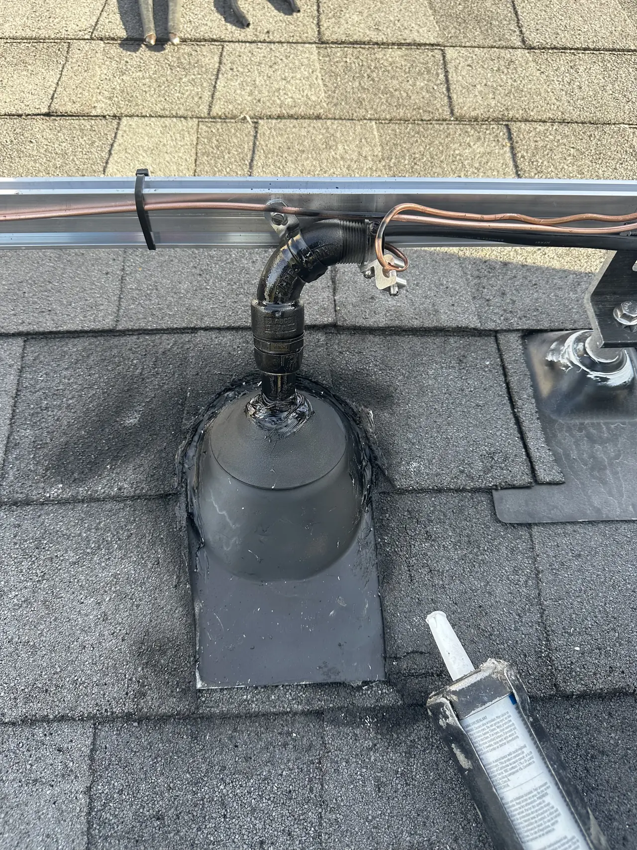 Conduit coming up through a sealed rubber boot on a dark shingle roof beside a solar rail, Hidden Hills