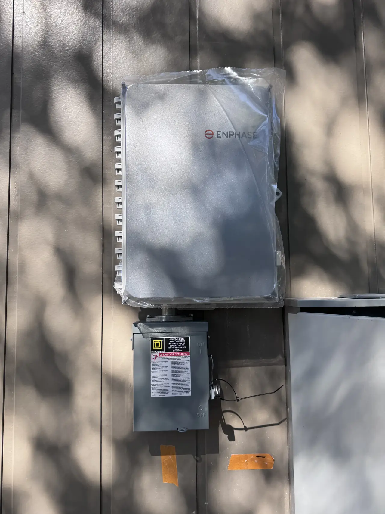 An Enphase combiner box and an AC disconnect mounted on the siding of a new house, Hidden Hills