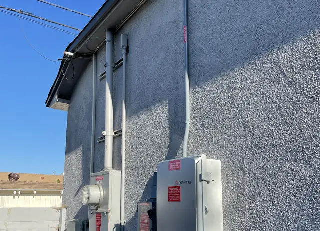 New solar service equipment mounted along a stucco wall under the eaves, with the sky above, Long Beach