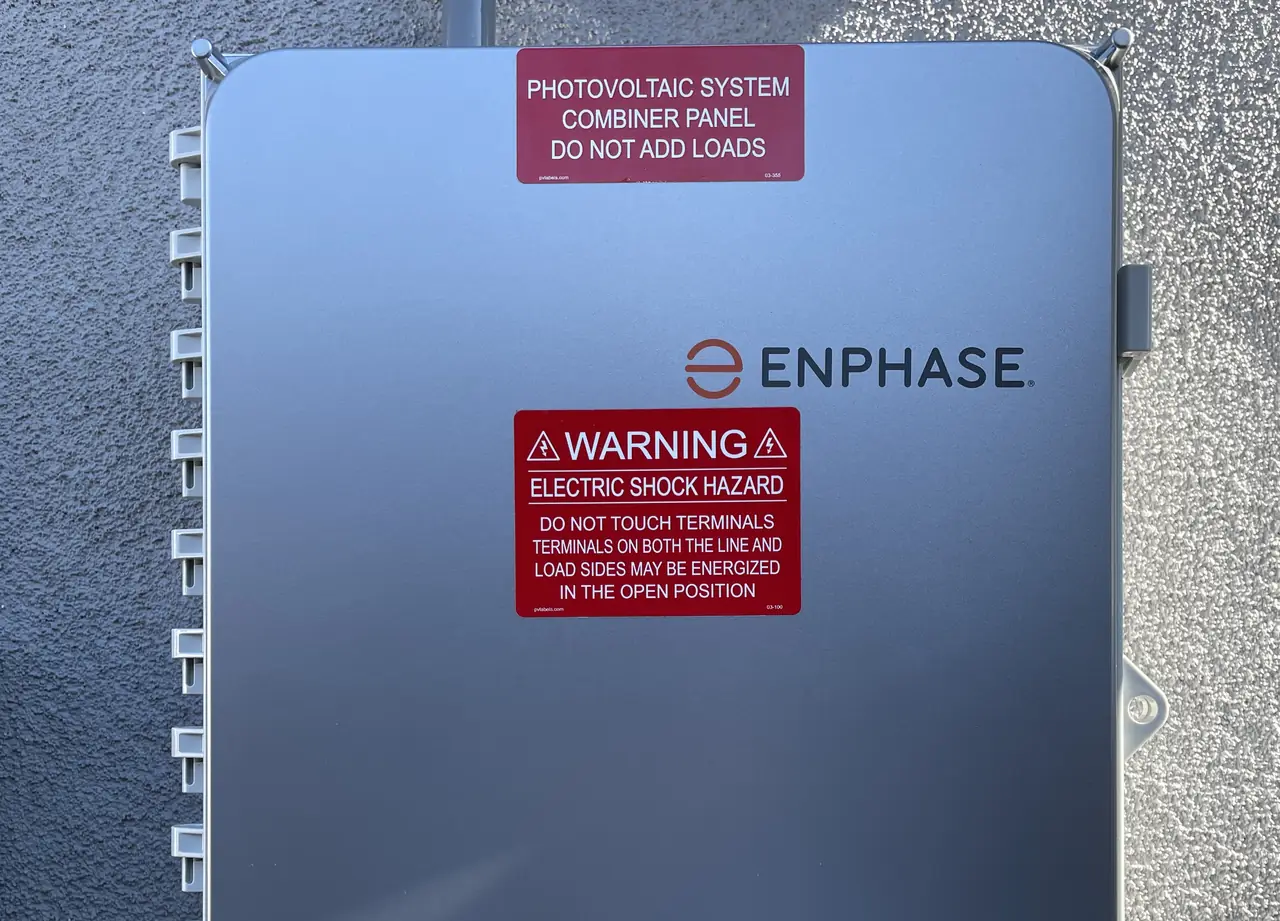 A closed solar combiner panel on a stucco wall with its warning placards, Long Beach
