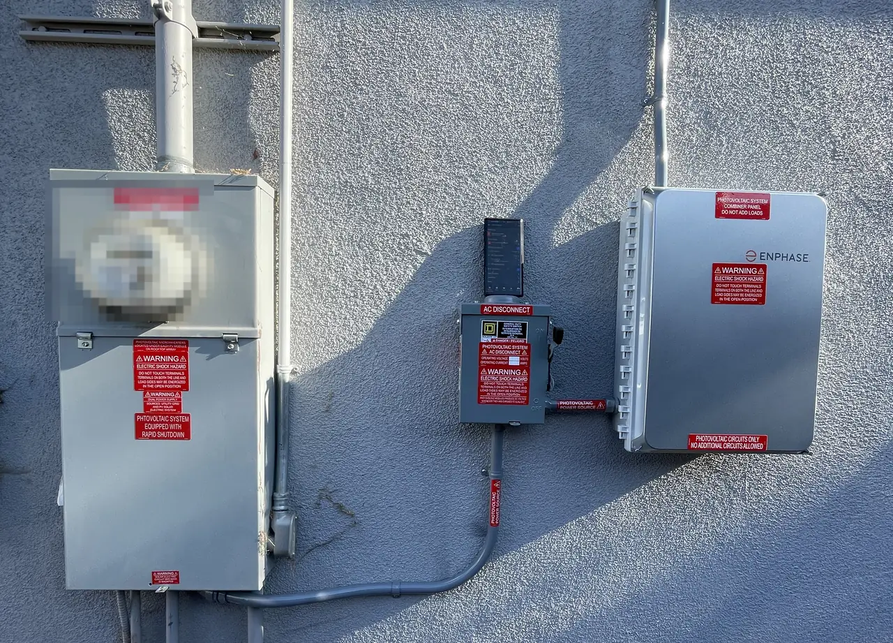 A meter enclosure, an AC disconnect and a combiner panel in a row along a stucco wall, Long Beach