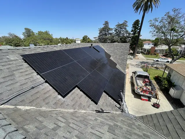 Black solar modules in separate groups across the faces of a steep hip roof with the street beyond, Long Beach