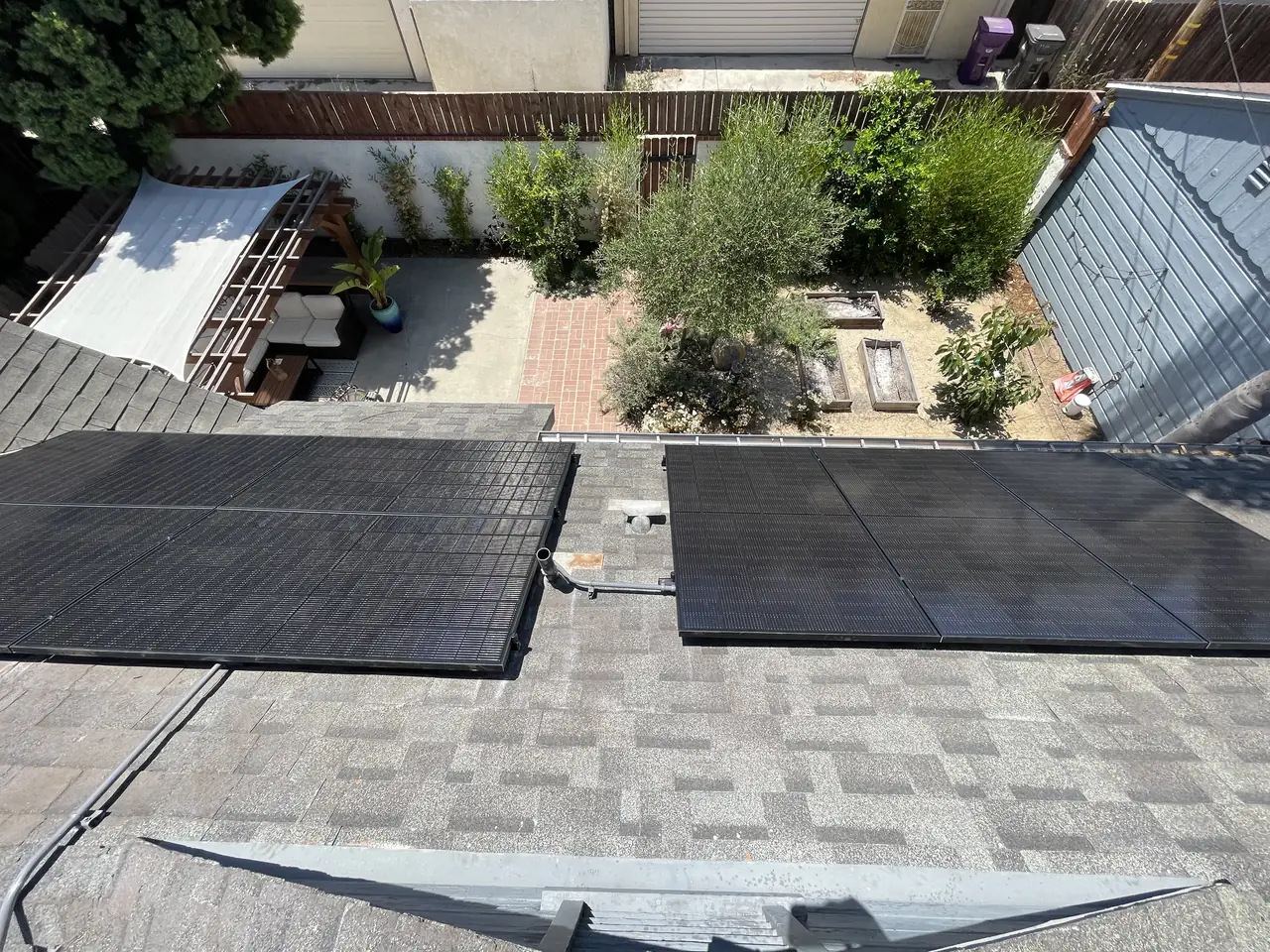 Two groups of solar modules on roof faces above a paved yard, with a roof vent between them, Long Beach