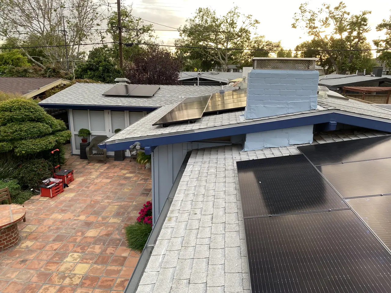 Groups of solar modules on the low roofs of a mid-century house seen from the ridge, with a courtyard below, Long Beach