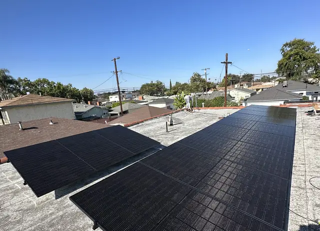 A tilted solar array raised on standoffs above a flat roof with the neighborhood beyond, Long Beach