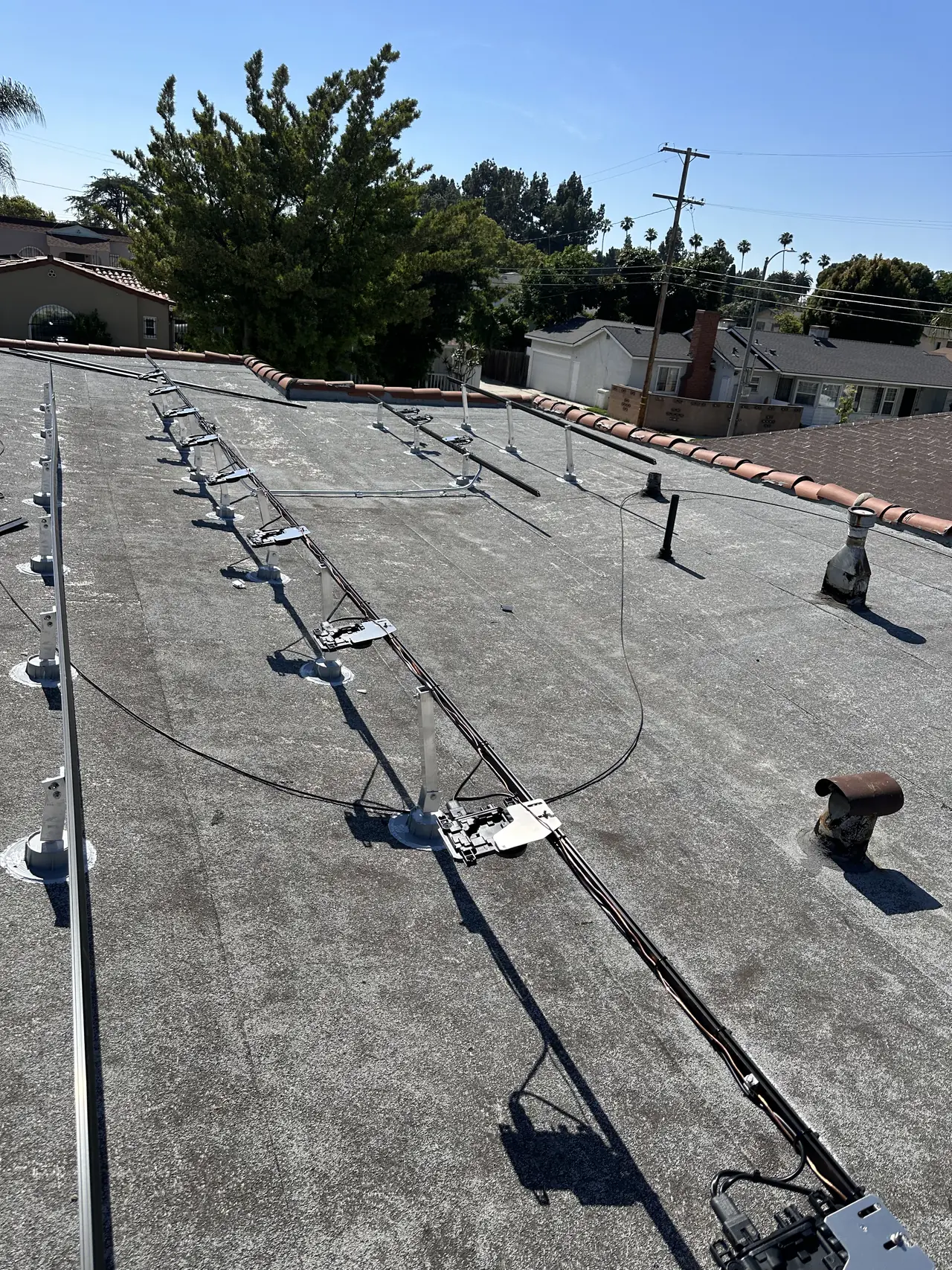 Aluminum rails and standoff bases laid out across a flat roof before the modules go on, Long Beach