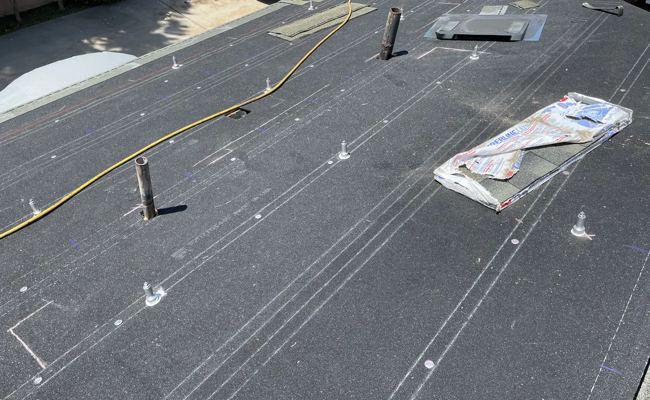 A stripped roof deck covered in underlayment with chalk lines and flashed mounting feet standing on it, Long Beach