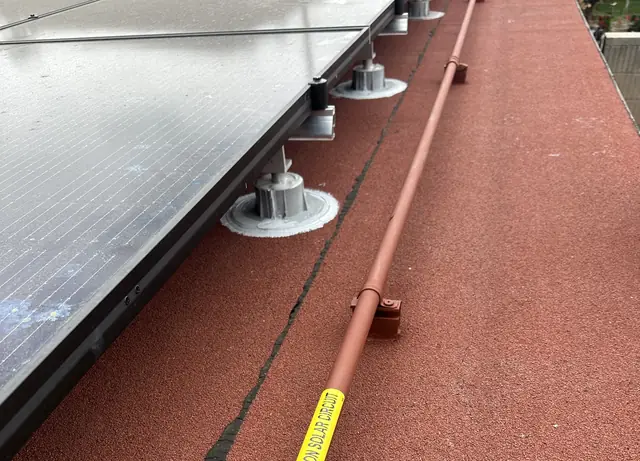 Solar modules on sealed standoffs above a red coated flat roof with the conduit run beside them, Long Beach