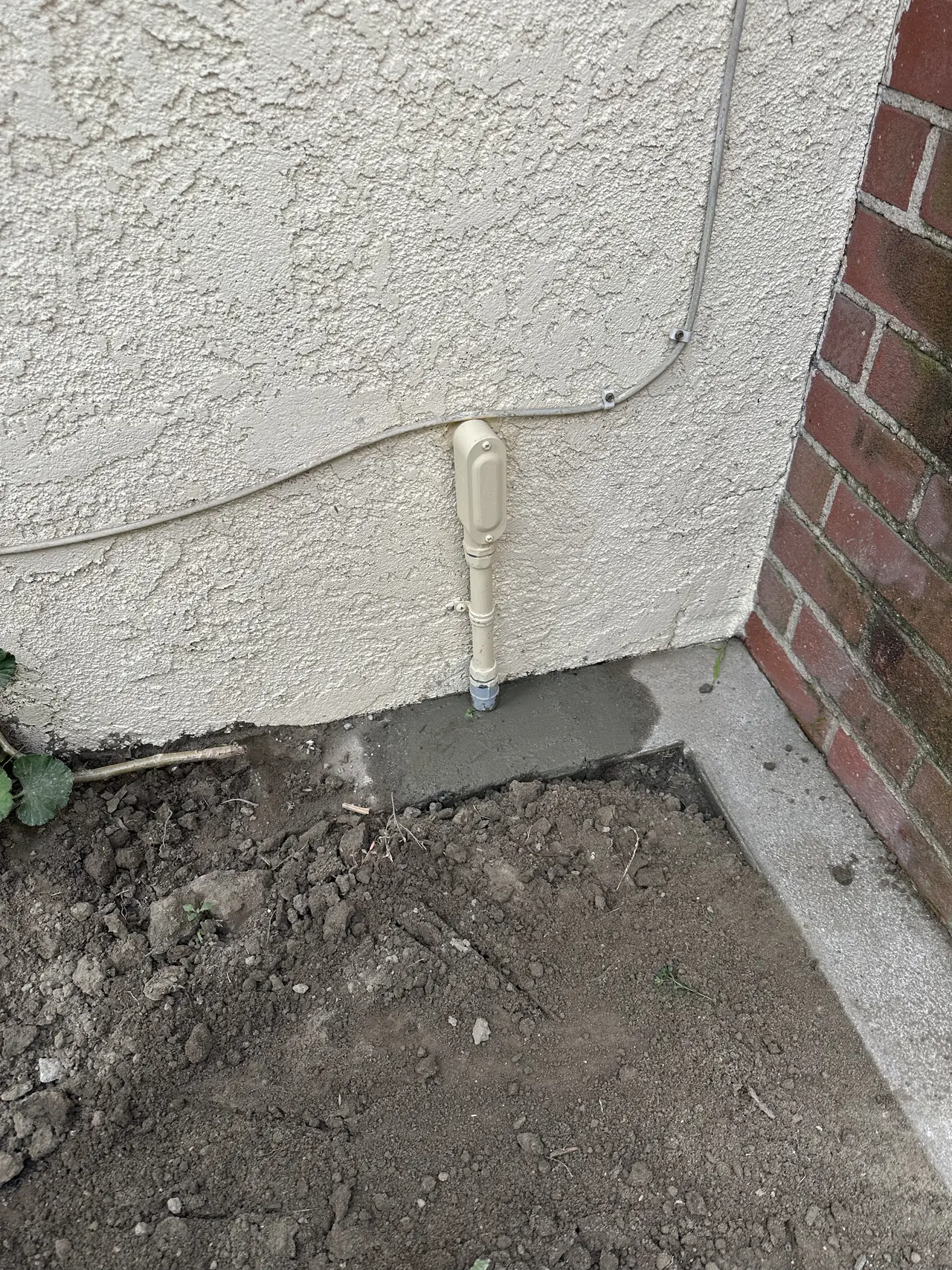 A painted conduit stub rising out of freshly backfilled ground at the base of a stucco wall, Long Beach