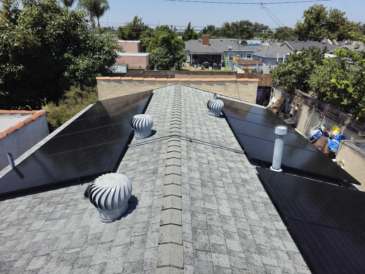 Flush solar modules on both slopes of a pitched shingle roof with turbine vents along the ridge, Long Beach