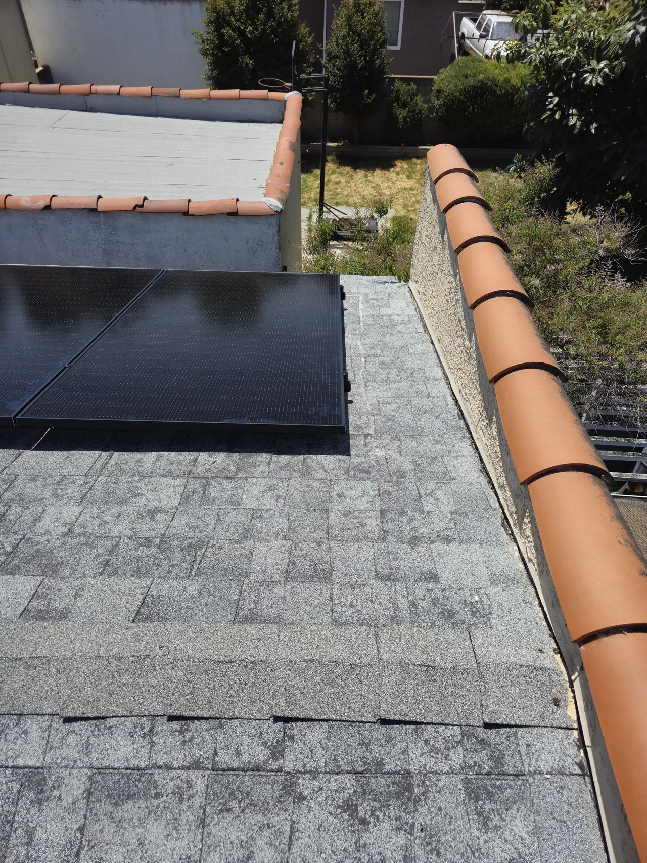 Flush solar modules on a shingle slope beside a tile ridge and a wall, Long Beach