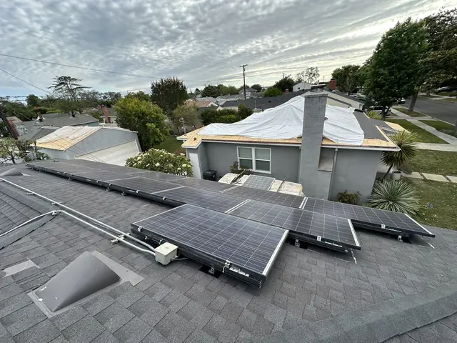 A reinstalled solar array back on a shingle hip roof in the evening light, with the neighborhood beyond, Long Beach