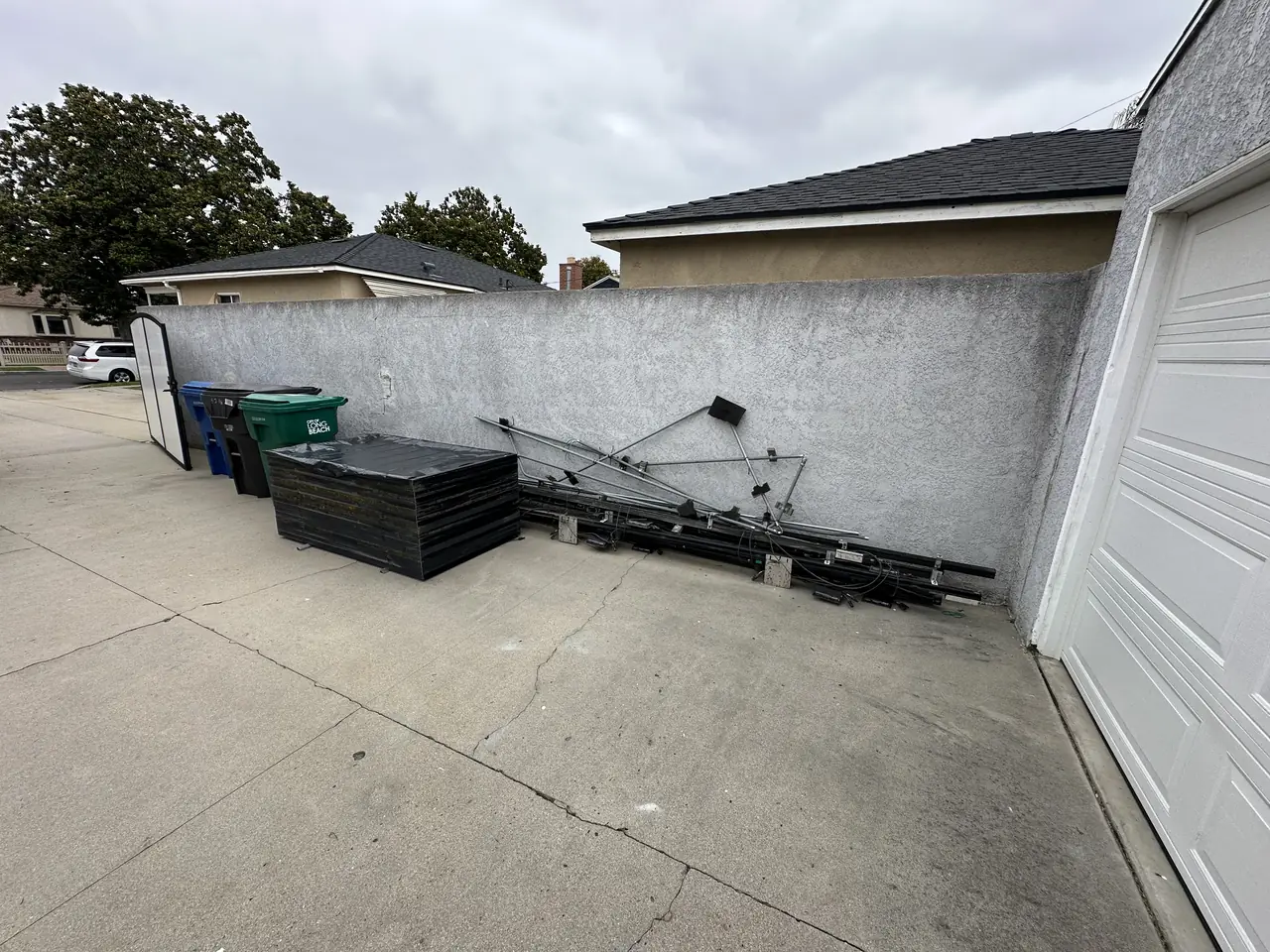 A solar array stacked face down on a driveway with the old racking leaning against the wall beside it, Long Beach