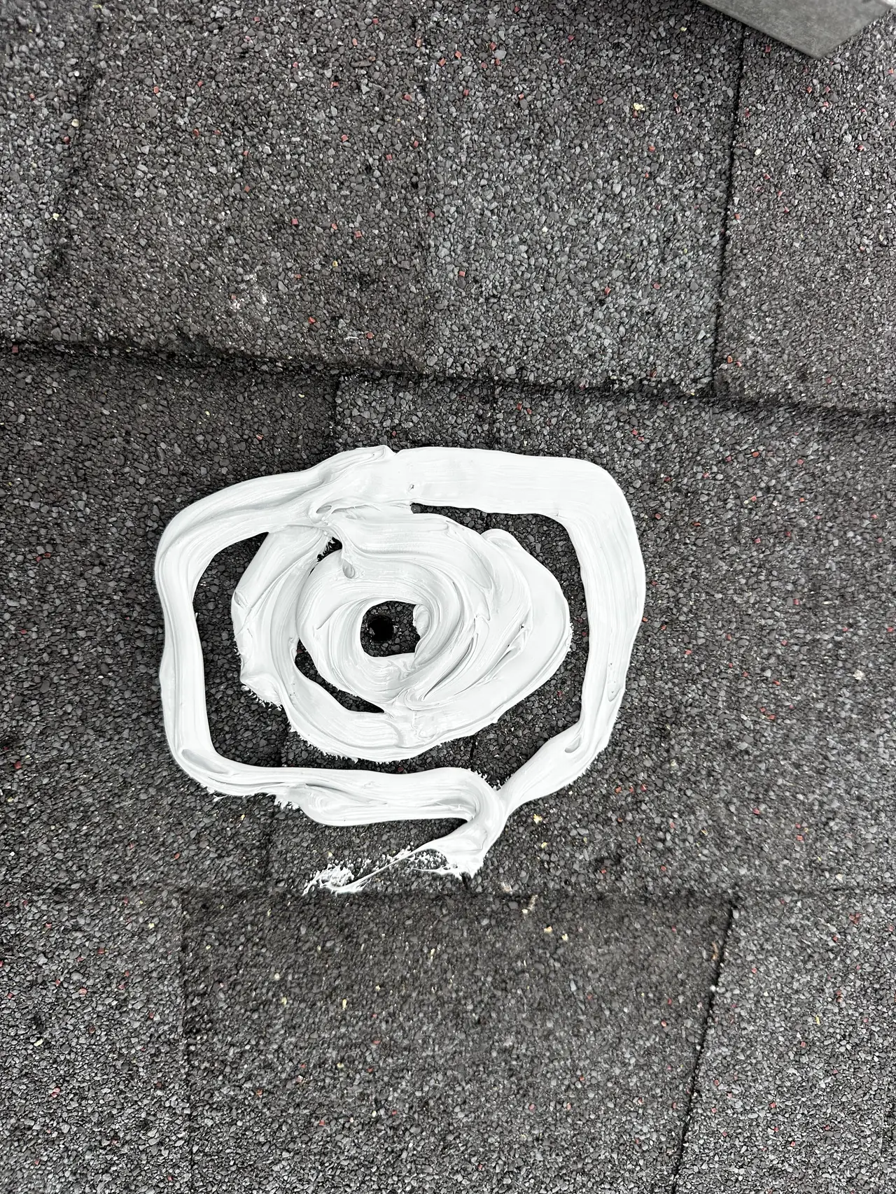 A lag hole in a new shingle roof bedded in a thick collar of white sealant before a new mount goes over it, Long Beach