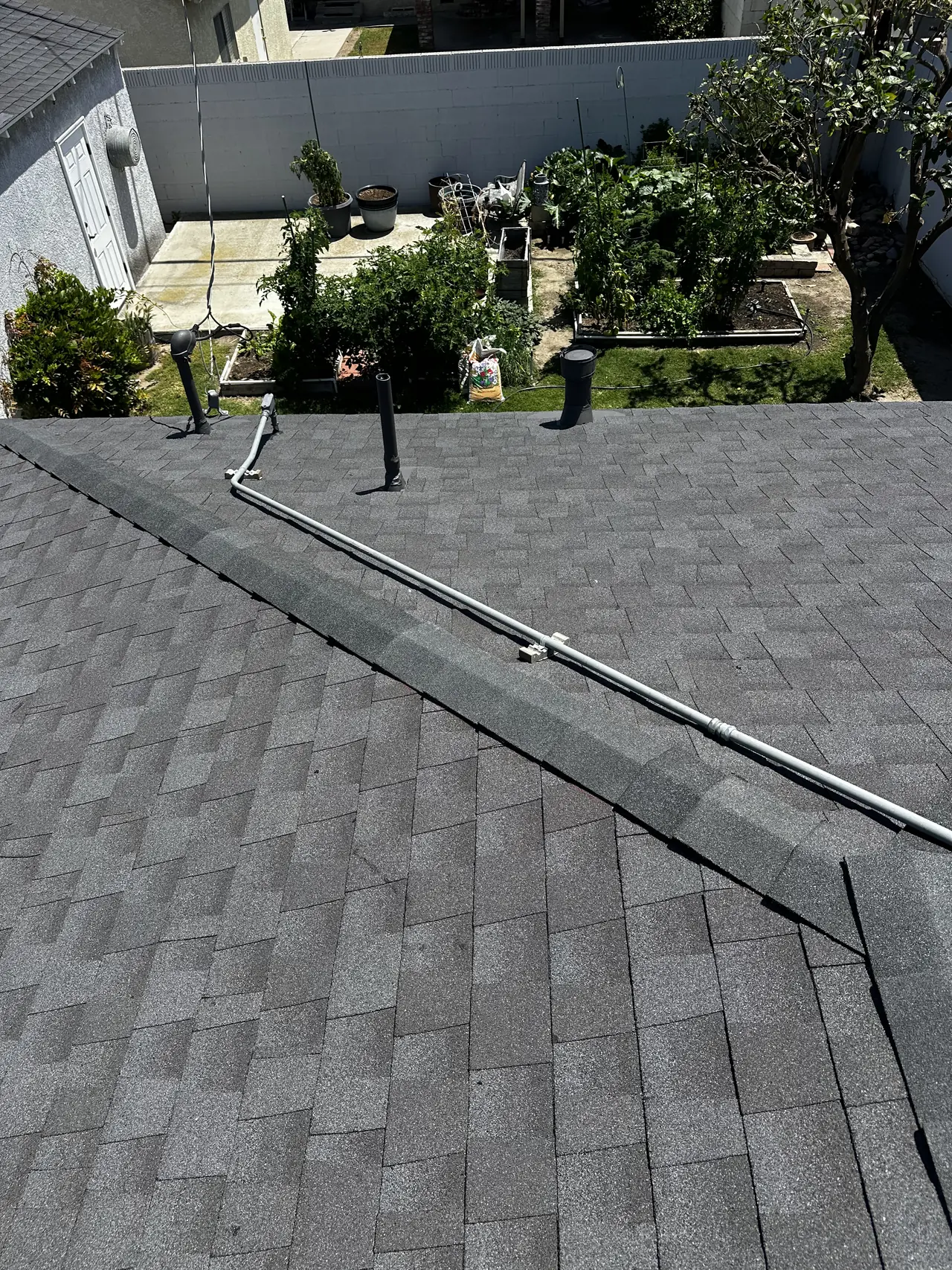 A shingle hip roof stripped of its solar array with a new conduit run along the ridge, Long Beach