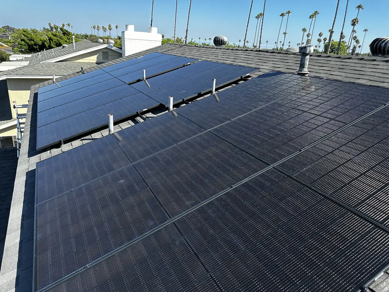 A black solar array across the slope of a composition shingle roof with the neighborhood beyond, Long Beach