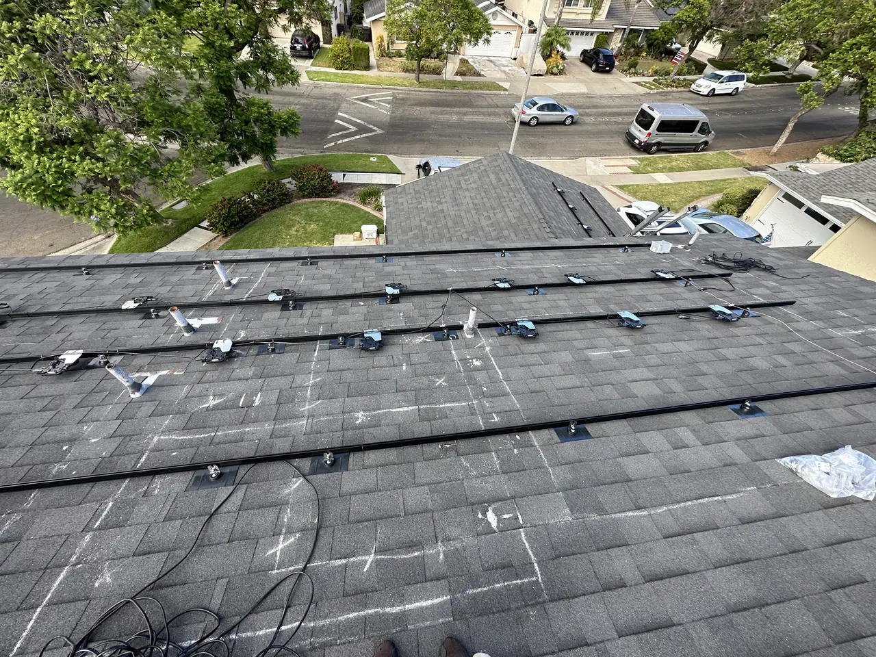 Aluminum rails and mounting hardware set out in rows across a bare shingle roof before the modules go on, Long Beach