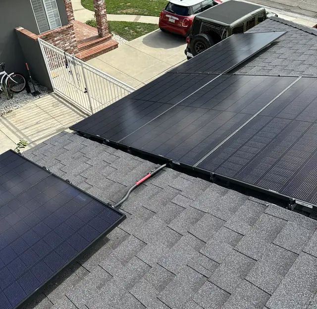 A solar array across the slope of a composition shingle roof with houses beyond, Long Beach