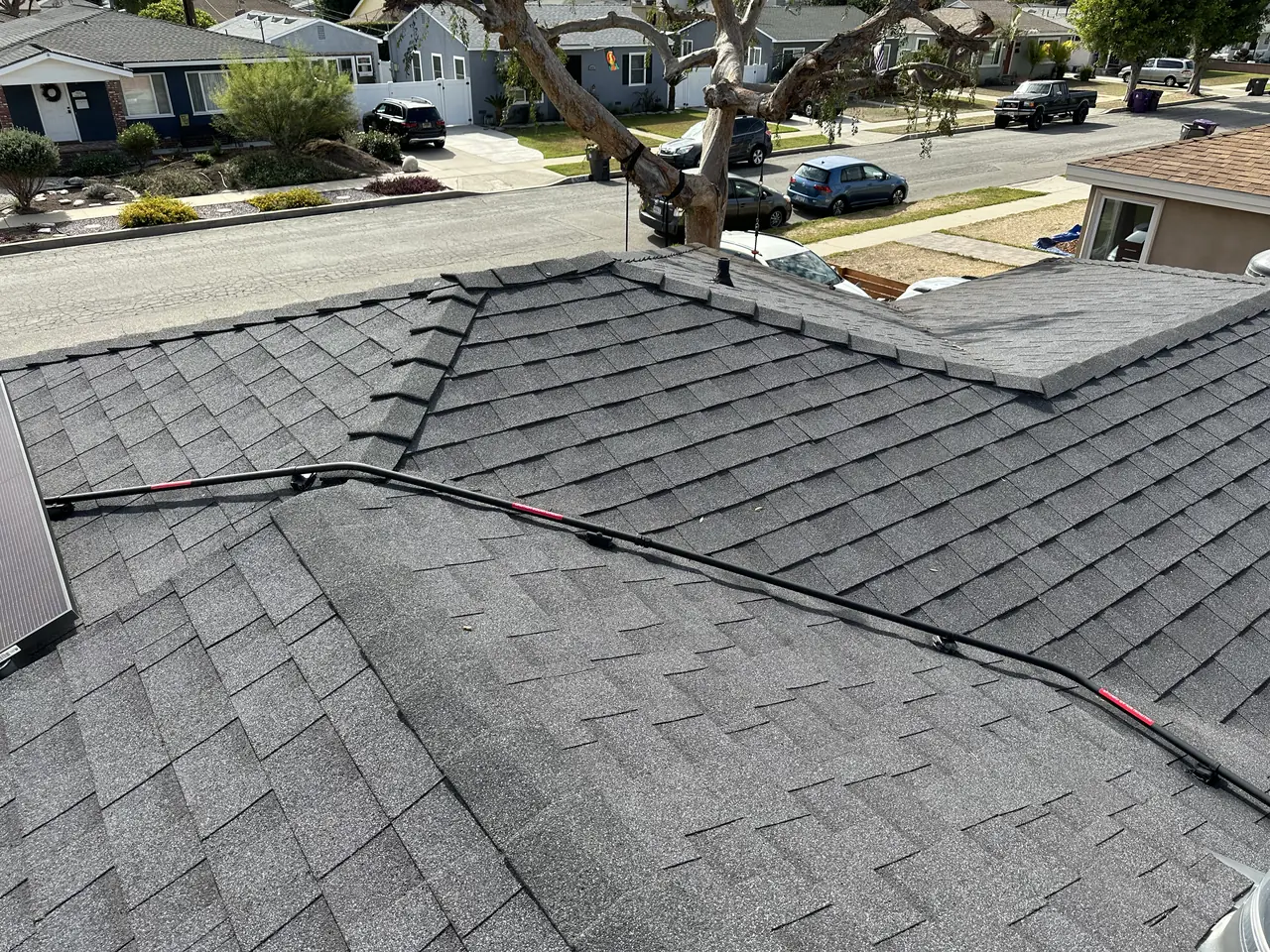 A solar array on a shingle roof seen along the ridge, with the street and neighboring roofs beyond, Long Beach
