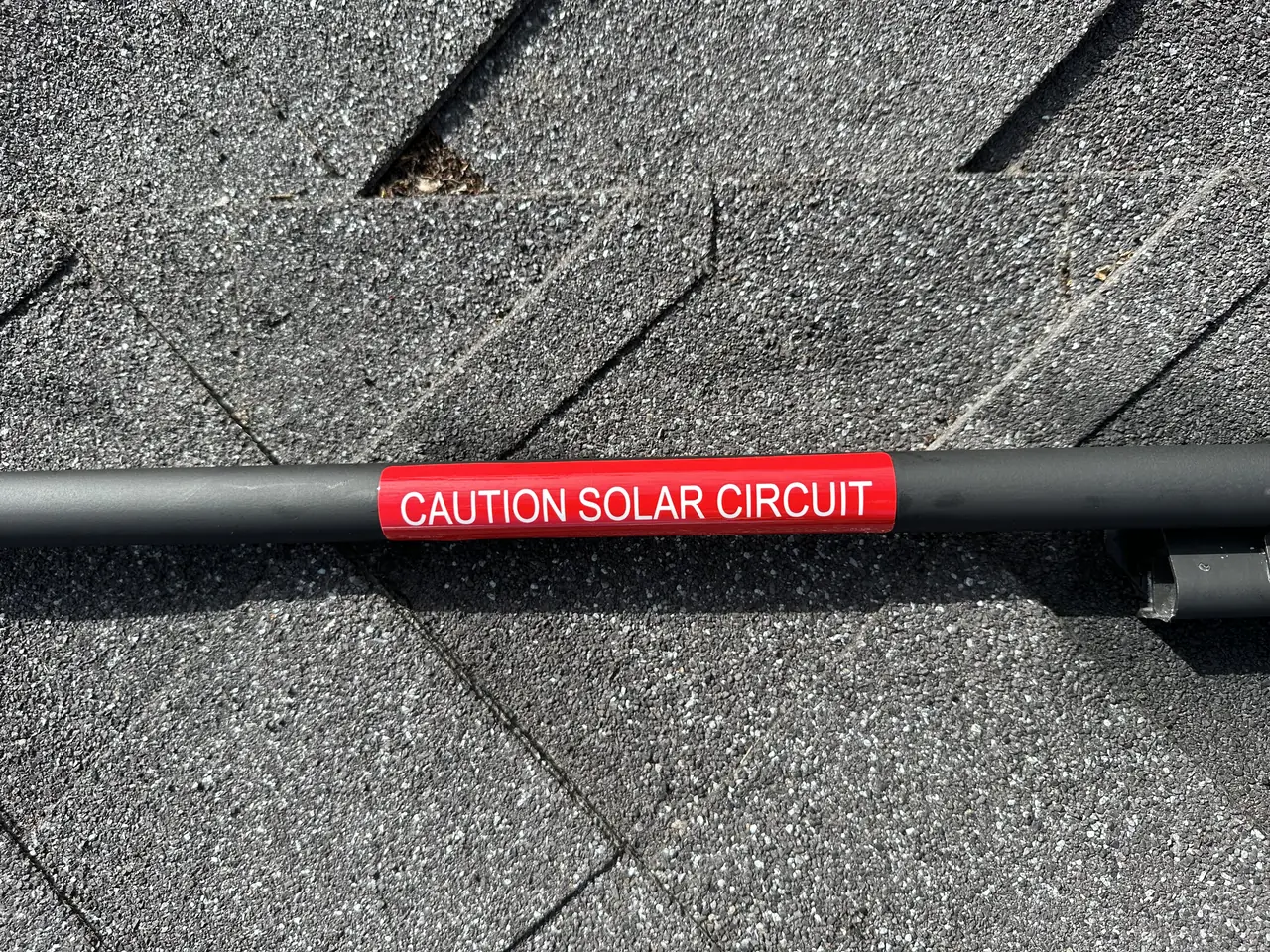 Conduit with a red caution solar circuit label running across a shingle roof, Long Beach