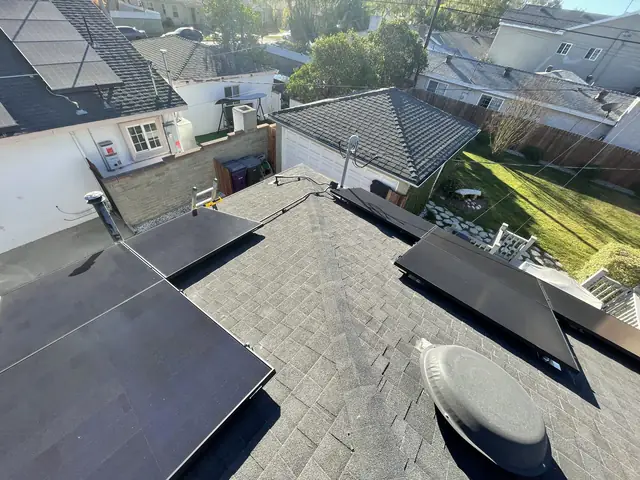 Two groups of solar modules on a shingle roof with the neighborhood and power lines beyond, Long Beach
