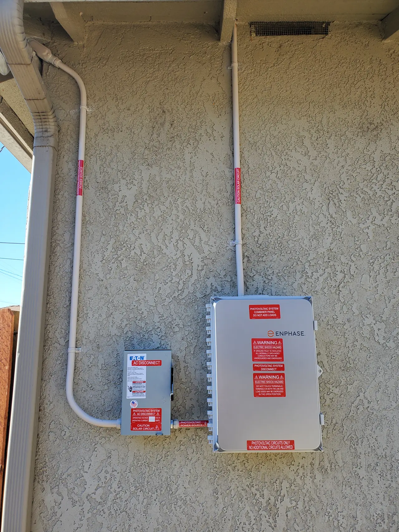 A disconnect and conduit run mounted on a stucco wall beside a fence, Long Beach
