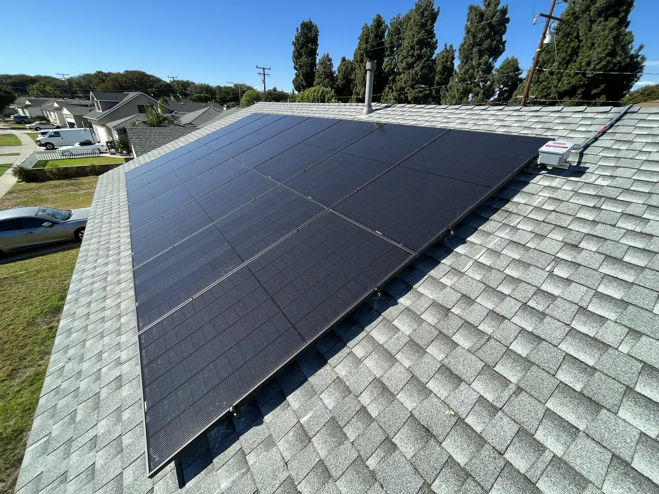 A solar array on a shingle roof seen along the ridge with houses and trees beyond, Long Beach