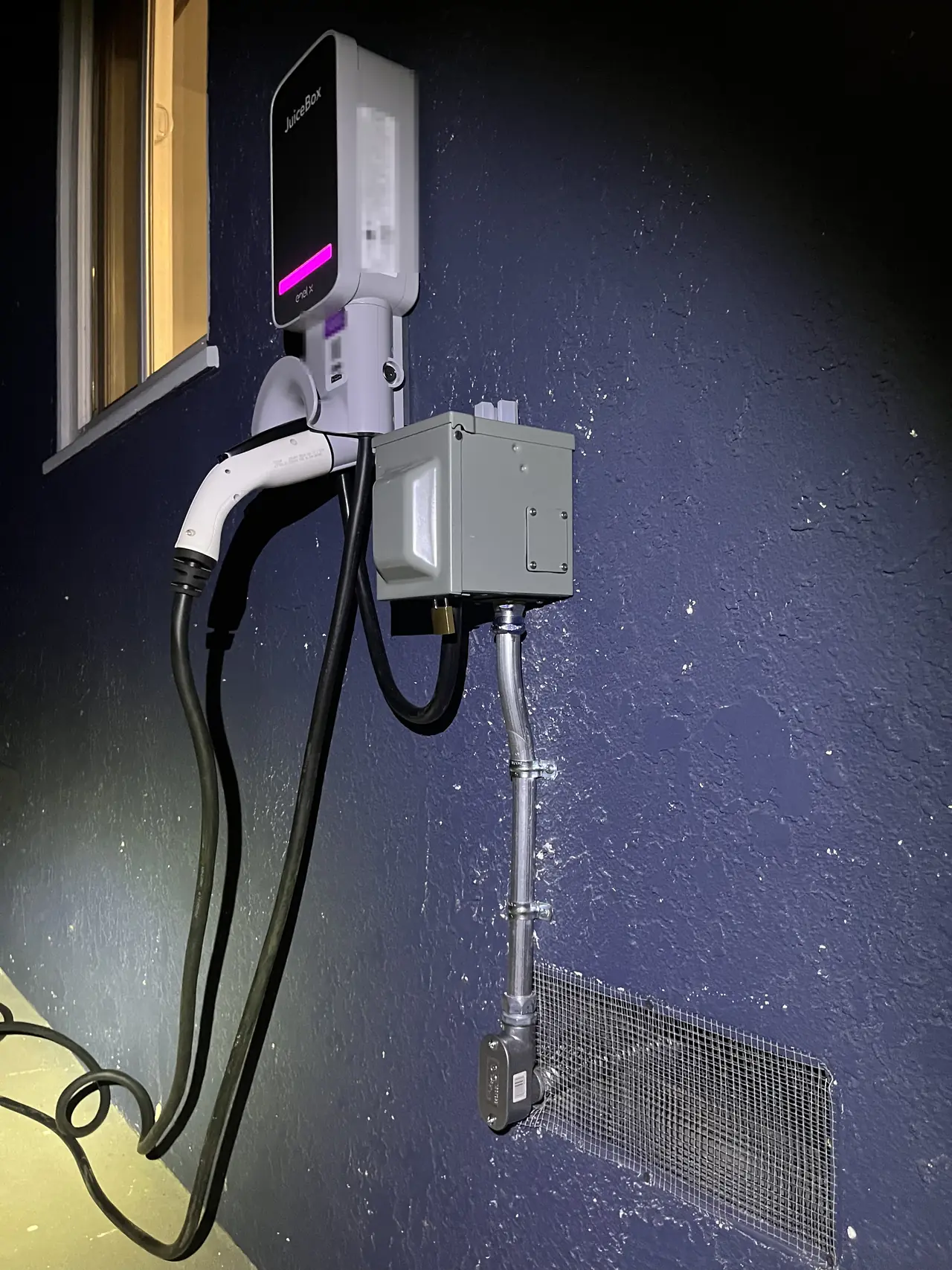 A wall-mounted car charger plugged into a fifty-amp outlet beside a doorway, with conduit running down the wall, Long Beach