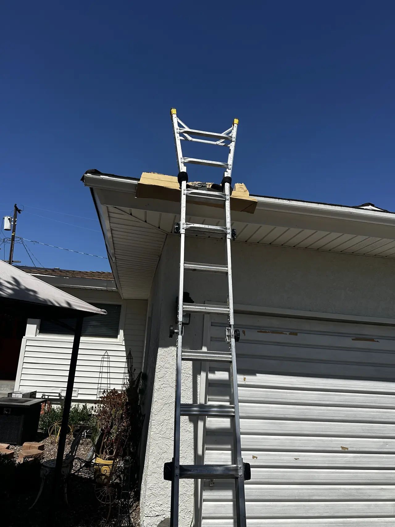 An aluminum ladder extending past a roof edge and bearing on a board laid over the gutter, Long Beach