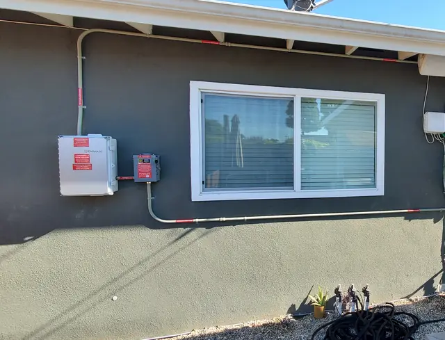 A finished conduit run crossing a stucco elevation below a window between the combiner and the service equipment, Long Beach