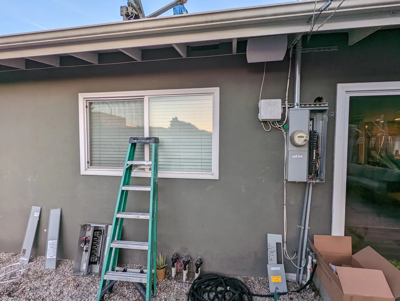 A stucco elevation with service equipment and a ladder leaning against the wall before the conduit run, Long Beach