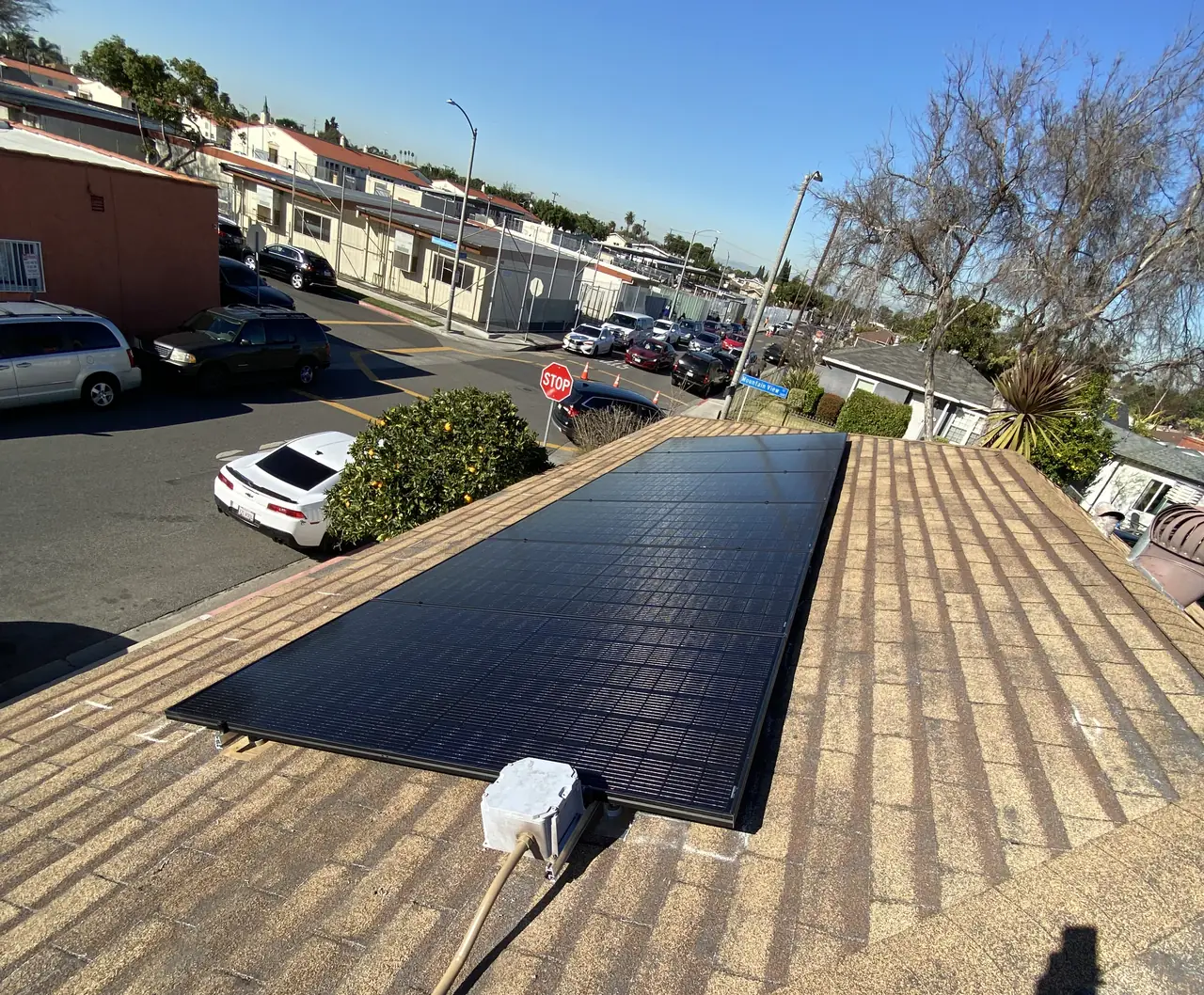 A short run of solar modules on a shallow tan shingle roof above a street, Long Beach