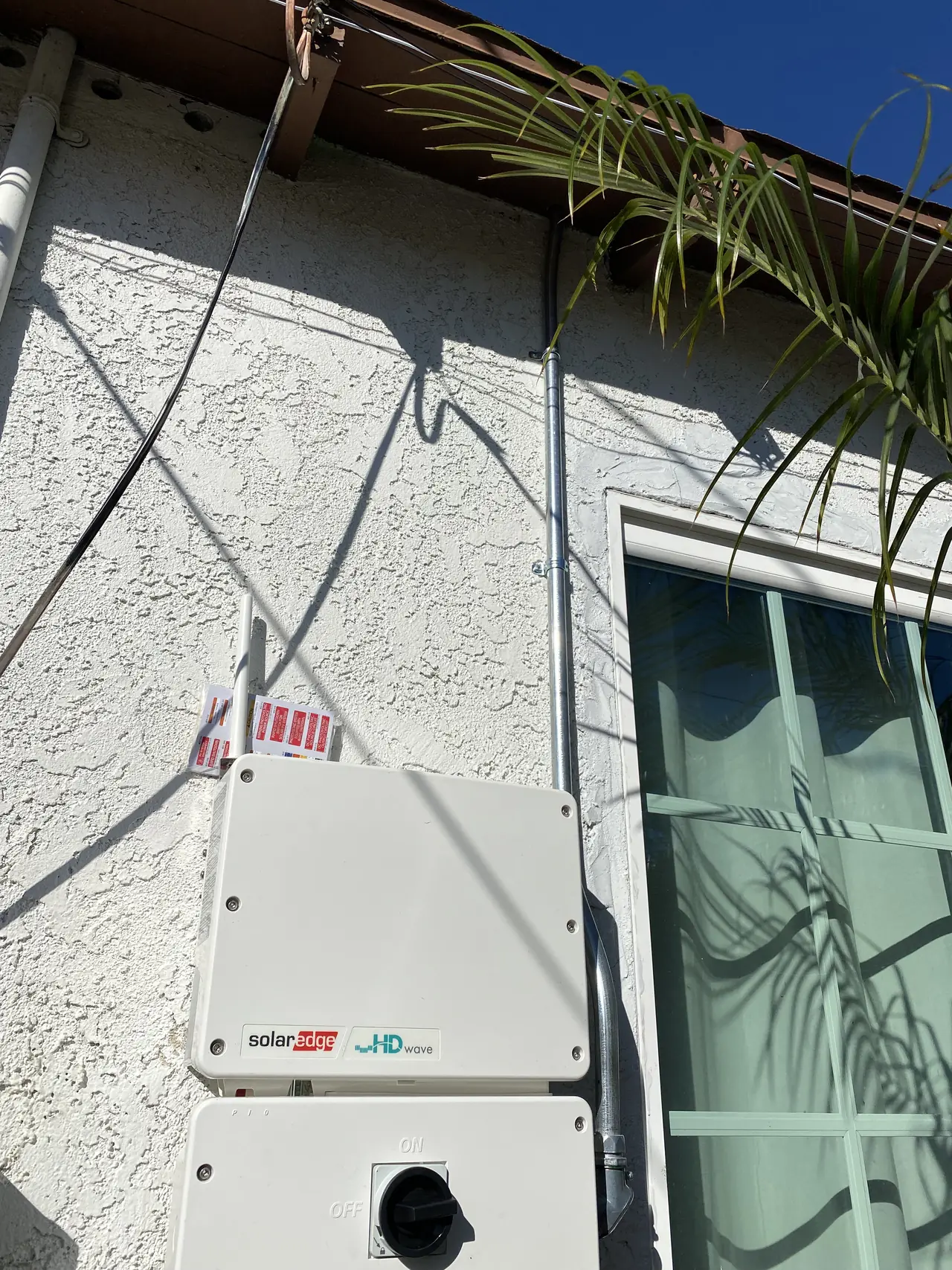 A wall-mounted inverter and disconnect on a stucco elevation beside a window, Long Beach